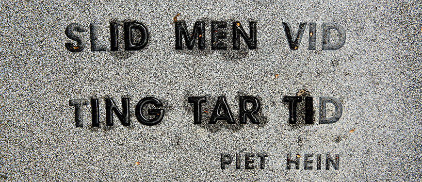 Billede af Piet Hein-citatet: Slid men vid ting tar tid. Citatet er fra et trin i trappeanlægget omkring Jørn Larsens kunstværk "Interstitiel", der er en 19 meter høj granitsøjle, der knejser på forpladsen til universtitetet på Campusvej.