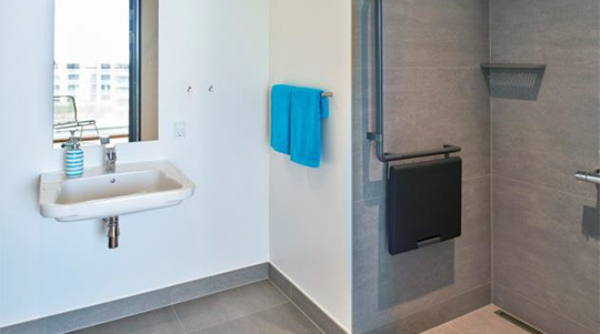 The image shows the bathroom with a sink and mirror to the left and shower stall to the right.