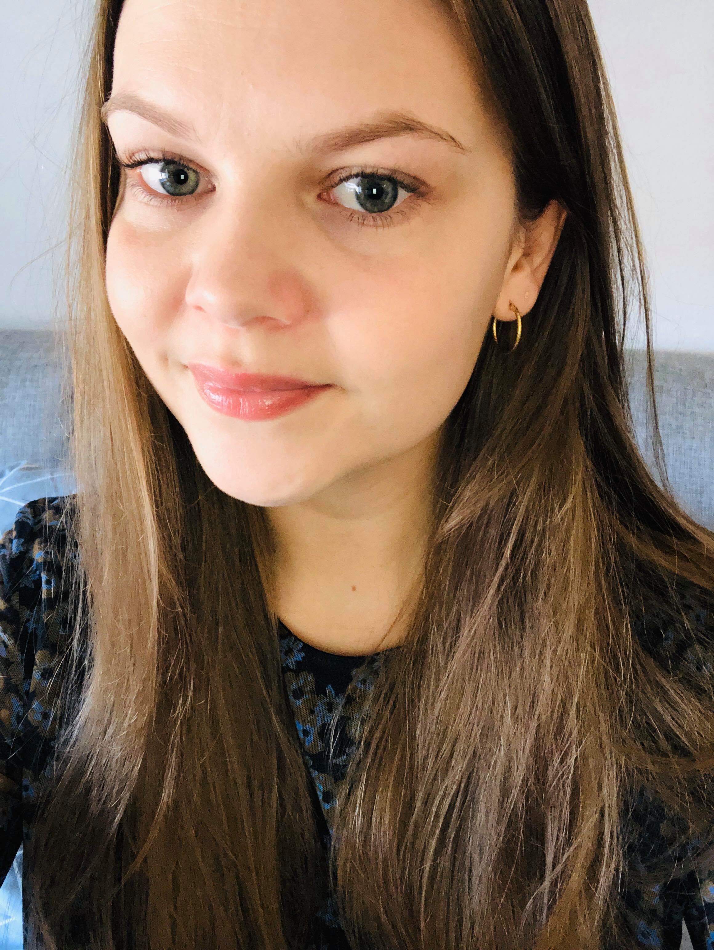 Nærbillede af en kvinde med langt brunt hår, lyse øjne og en guldring i øret.